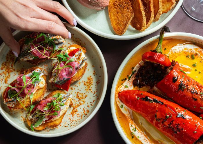 A hand picking up a tapa of seafood on tasted bread with other brightly coloured food plates at The Sydney Connection, Potts Point