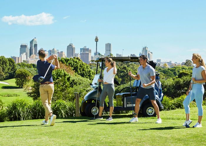 Four people teeing off with Sydney's city skyline in the background at Moore Park Golf Course, Moore Park