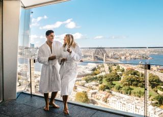 Couple enjoying a coffee and harbour views from their luxurious Crown Towers hotel suite at Crown Sydney, Barangaroo