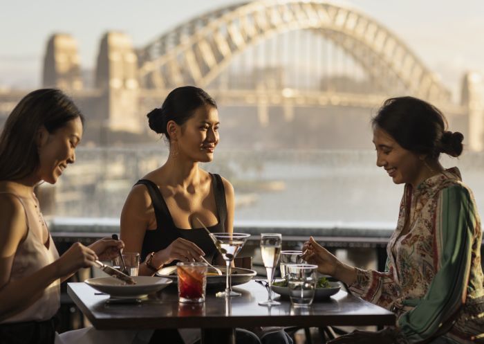 Friends enjoying food and drink with views across Sydney Harbour at Cafe Sydney, Sydney City
