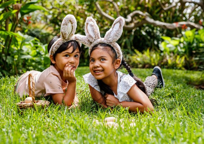 Two children lying on grass wearing fluffy bunny ears at Vaucluse House