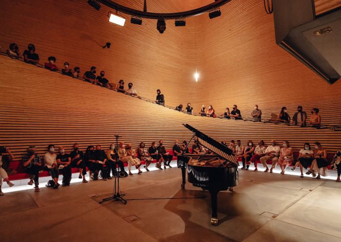 A grand piano sits in a large performance space as people gather for Phoenix's Fazioli pianoforti - Phoenix Central Park, Chippendale