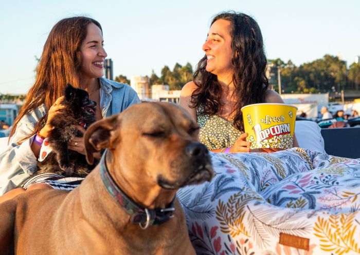 Friends cosying up with a snack with their pooch pals, Mov'in Bed Beach Cinema, Barangaroo