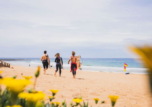 Three surfers heading to beach, North Narrabeen Beach, North Narrabeen