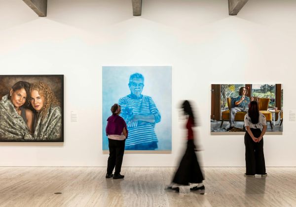 Visitors walking past artworks the Archibald Wynne and Sulman Prizes 2025 Exhibition