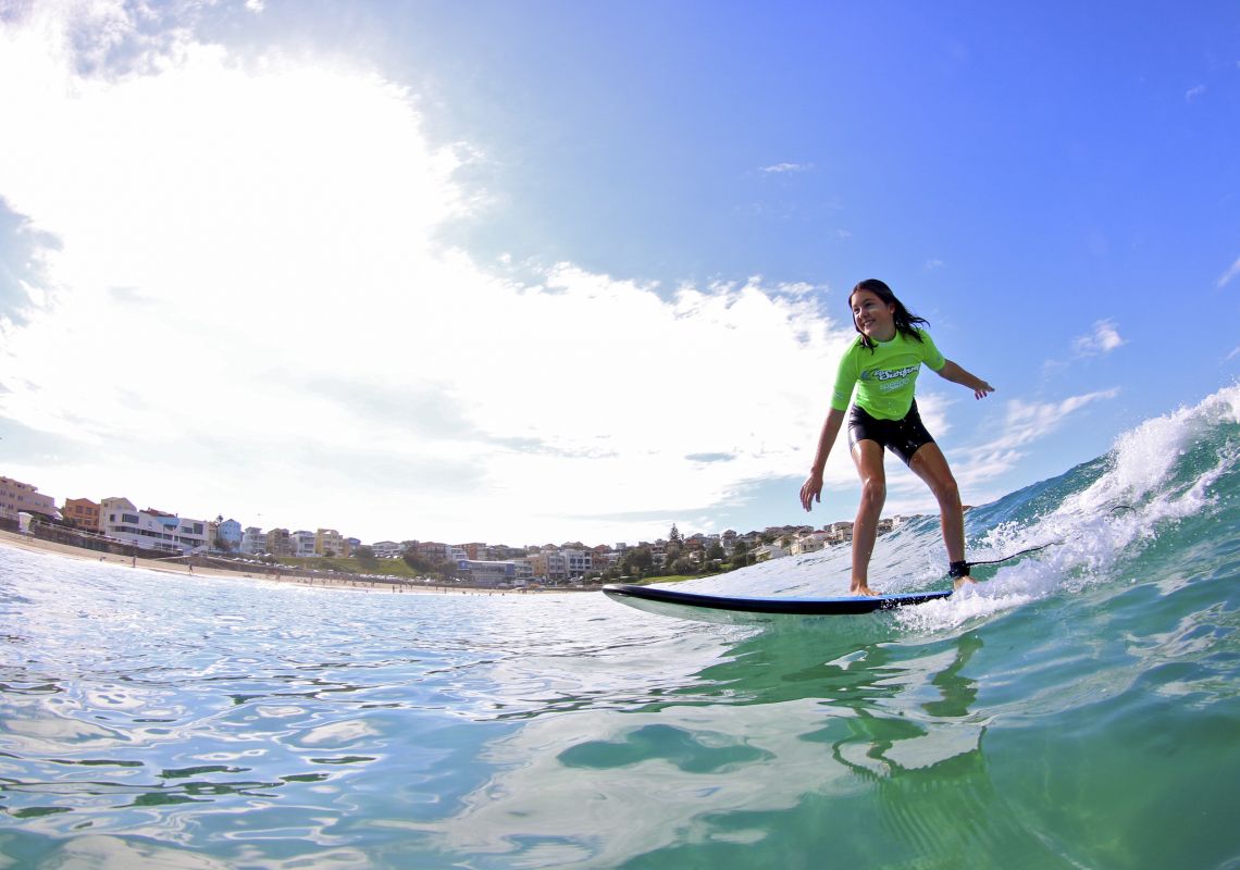 Girl catching a wave at Bondi Beach with surf school Lets Go Surfing