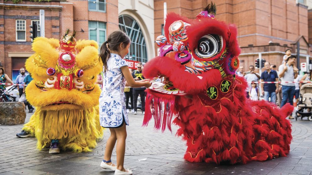 Young girl places a red packet into the mouth of the dragon during Chinese New Year in Chinatown, Sydney City