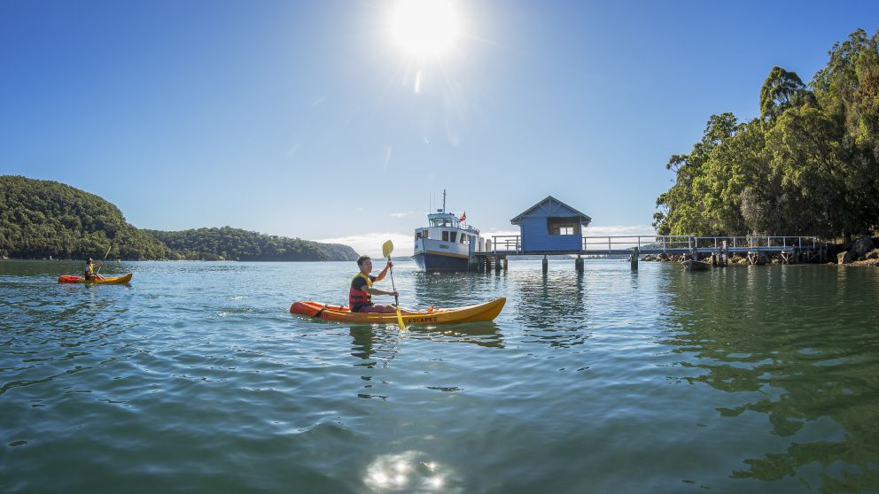 Friends kayaking on Pittwater as a ferry arrives at Bennetts Wharf, Coasters Retrea, Sydney