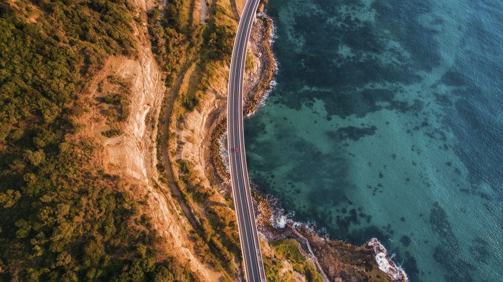 Aerial overlooking cars driving along Sea Cliff Bridge in Clifton, Illawarra