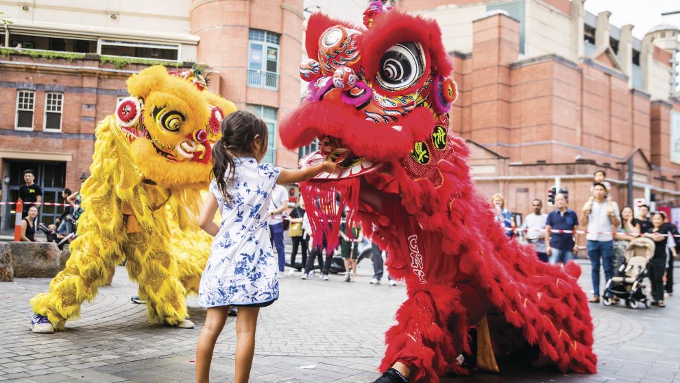 Young girl places a red packet into the mouth of the dragon during Chinese New Year in Chinatown