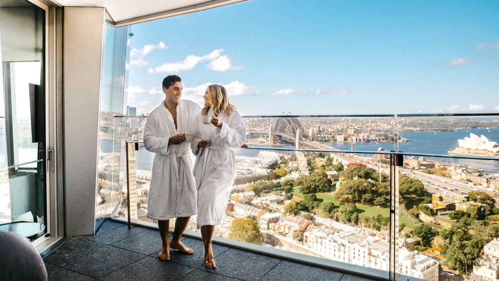 Couple enjoying a coffee and harbour views from their luxurious Crown Towers hotel suite at Crown Sydney, Barangaroo