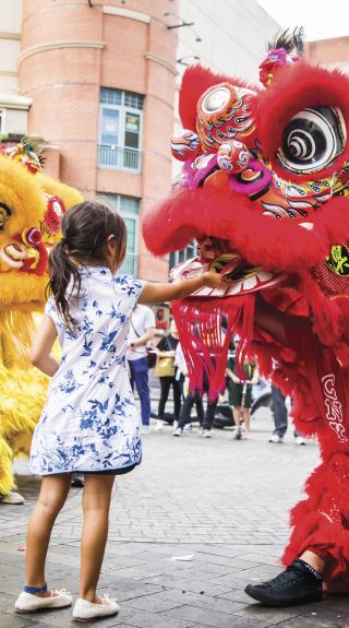 Young girl places a red packet into the mouth of the dragon during Chinese New Year in Chinatown