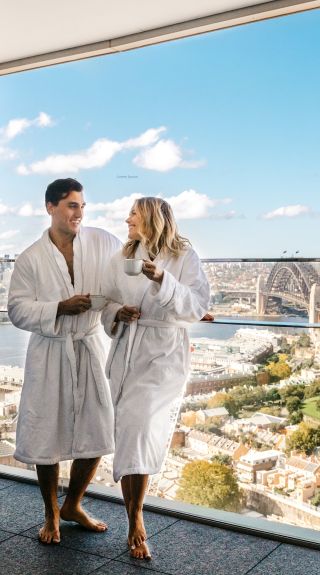 Couple enjoying a coffee and harbour views from their luxurious Crown Towers hotel suite at Crown Sydney, Barangaroo