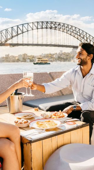 Couple enjoying food and drink with harbour views, Opera Bar, Sydney