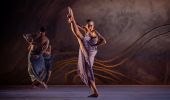A dancer in a purple dress lifting her leg on stage with two dancers in the background, Bangarra Dance Theatre, Dawes Point - Credit: Daniel Boud