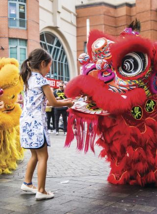 Young girl places a red packet into the mouth of the dragon during Chinese New Year in Chinatown, Sydney City