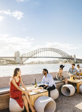 Couple enjoying food and drink with harbour views at Opera Bar, Sydney.