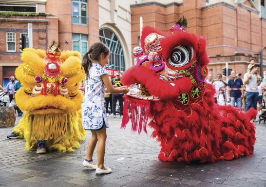 Young girl places a red packet into the mouth of the dragon during Chinese New Year in Chinatown, Sydney City