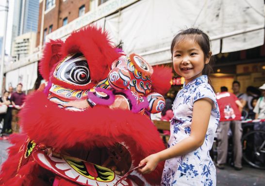 Young girl places a red packet into the mouth of the dragon during Chinese New Year in Chinatown, Sydney City