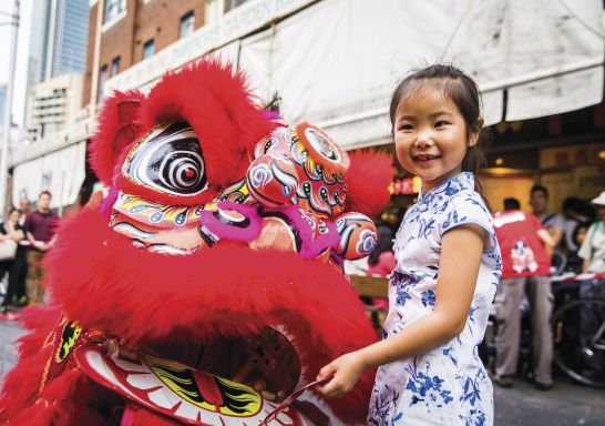 Young girl places a red packet into the mouth of the dragon during Chinese New Year in Chinatown, Sydney City