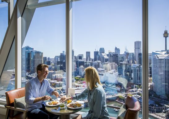 Couple enjoying food and drink at Club Millésime inside Sofitel Sydney Darling Harbour.