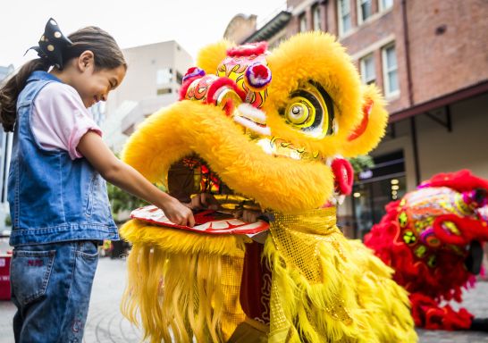 Young girl places a red packet in mouth of the dragon for Lunar New Year, Chinatown